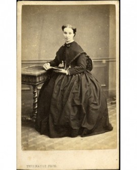 Femme en robe assise devant une table, tenant un livre ouvert