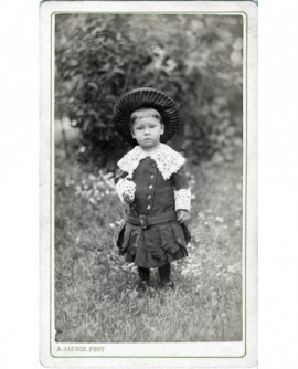 Enfant en robe et chapeau de paille debout dans un jardin