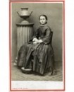 Femme en robe assise, colonne surmontée d\'un vase