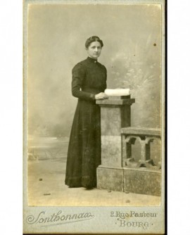 Femme en robe noire debout, tenant un livre sur un piédestal