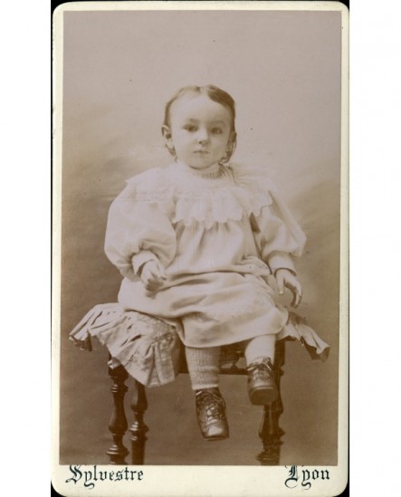 Bébé en robe et en souliers assis sur un tabouret