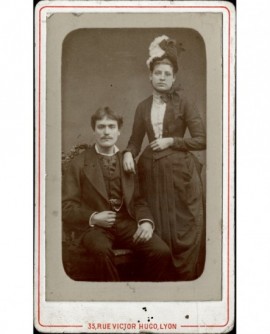 Couple- homme assis et femme en chapeau debout