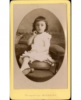 Petite fille en robe blanche assise sur une chaise