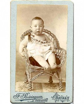 Bébé en chemise, épaule dénudée, assis sur une petite chaise
