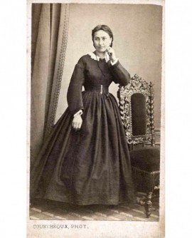 Jeune femme debout, accoudée à une chaise,la main gauche soutenant sa tête