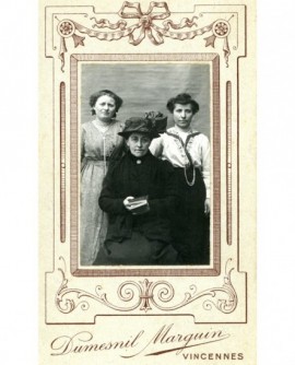 Trois femmes, la plus âgée devant en chapeau, livre à la main