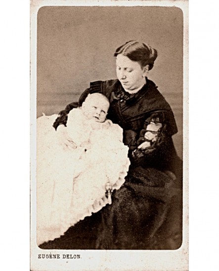 Jeune femme en noir tenant un bébé en robe (de baptême)