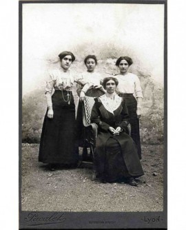 Femme en robe assise, mains jointes, entourée de trois jeunes filles en corsage blanc